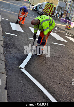 Workman applying hot white road line marking paint on zebra-stripe and pedestrian cross-walk on newly surfaced road Stock Photo