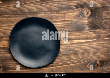 black ceramic plate with an irregular edge on a grained wood  with a copy space Stock Photo