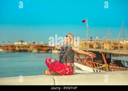 Tourism in qatar. Happy caucasian woman enjoying along Corniche promenade with Dhow Harbour on background. Lifestyle tourist in Doha city, Qatar Stock Photo