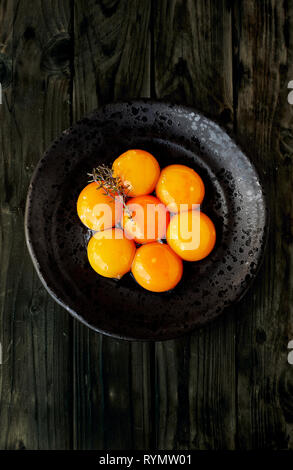 Seven Egg Yolks on a black rustic plate with a Sprig of Thyme (Thymus Zygis variety) over a wooden table. Stock Photo