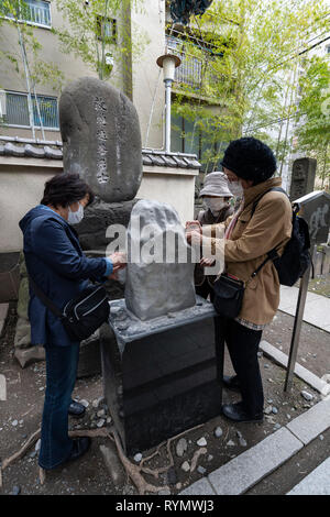 People scraping front stone of tomb of Nezumi Kozō Jirokichi, a Japanese thief and folk hero who lived in Edo, Ekō-in, Sumida-Ku, Tokyo, Japan Stock Photo