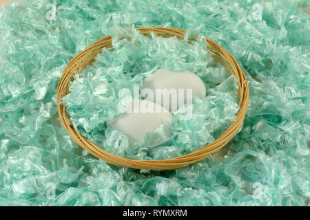 Two white eggs in wooden wicker basket surrounded by green fluffy yarn Stock Photo