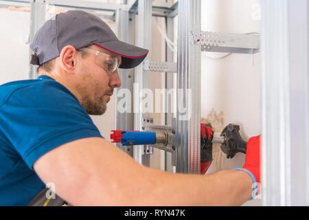 Plumbing Work. Caucasian Plumber in His 30s Installing Water Supply Inside Newly Remodeled Bathroom. Stock Photo