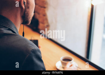 The man in headphones using mobile phone, sitting with coffee at cafe Stock Photo