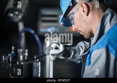Metalworking Technician at Work. Caucasian Factory Worker in Blue Hard Hat and Safety Glasses. Stock Photo
