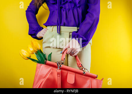 Studio shot of a young woman wearing spring outfit and holding a bag with yellow tulips on yellow background Stock Photo