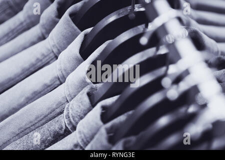 Row of denim jackets or shirts on black hangers, a top view closeup. Jeans wardrobe. Blue textile backgound, blurry (shallow depth of field). Stock Photo