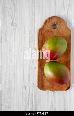 Mangoes on rustic wooden board on a white wooden table, top view. Flat lay, from above, overhead. Copy space. Stock Photo