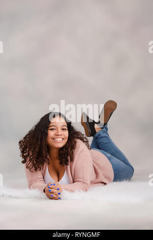 Attractive biracial high school senior laying down on floor smiling and posing for studio portraits Stock Photo