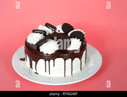 White whipped cream frosted cake with chocolate cream filled sandwich wafer cookies, melted chocolate melting down the sides on a porcelain plate, on  Stock Photo