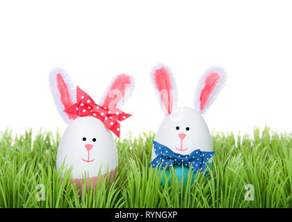 Easter Eggs crafted into bunnies, boy and girl, wearing bow tie and bow on ear sitting in green grass isolated on white background Stock Photo