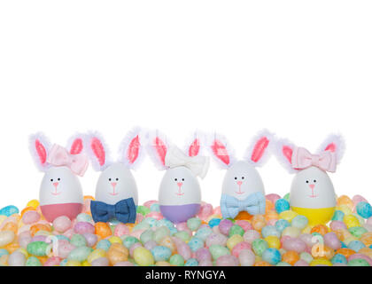 Easter Eggs crafted into bunnies, boys and girls, wearing bow ties and bows on ear sitting in pastel colored speckled jelly beans isolated on white Stock Photo