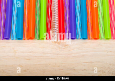 Row of colorful plastic and silicone reusable straws with cleaning brush in the middle laying on light wood table, viewed from above. Ecologically fri Stock Photo