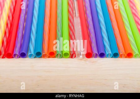 Row of colorful plastic and silicone reusable straws with cleaning brush in the middle laying on light wood table, viewed from above in front. Ecologi Stock Photo