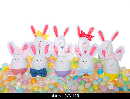 Two rows of Easter Eggs crafted into bunnies, boys and girls, wearing bow ties and bows on ear sitting in pastel colored speckled jelly beans isolated Stock Photo