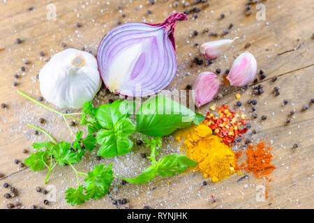 Food photography.Meal ingredients.Red onion, garlic bulbs, black pepper, freshly cut basil leaves and colourful spices placed on rustic wooden table. Stock Photo