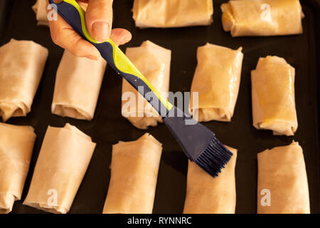 Woman's hand applying butter onto puff pastry cheese bites turnovers. Chef's hand baking close up puff pastry sheets cheese bites. Stock Photo