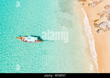 View from above, stunning aerial view of an empty beautiful tropical beach with white sand, turquoise clear water and a traditional long-tail boat. Stock Photo