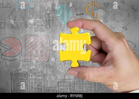 Hand holding gold jigsaw puzzle piece with business concept doodles wall background Stock Photo