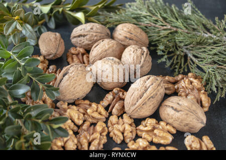 Walnut kernels near whole nuts on a dark, black background with green branches. Stock Photo