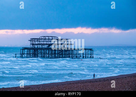 A person strolling on Brighton beach at sunset in front of the wreckage of the West Pier Stock Photo