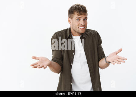 Have no idea. Unaware charismatic and cute fair-haired masculine male with bristle making shoulder shrugg with hands sideways and sorry smile as being Stock Photo