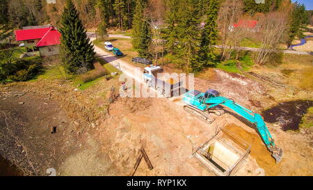 A backhoe digging a deep hole on a part inside the forest where there are lots of trees around Stock Photo