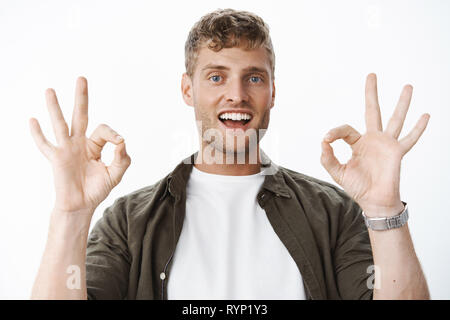 No problem got it. Portrait of carefree handsome blond man with bristle and blue eyes showing okay gestures and smiling satisfied as assuring things Stock Photo