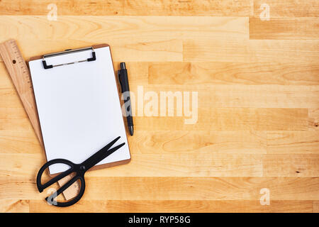 Cardboard clipboard, scissors, ruler and pen on yellow wood background. Top view. Copy space for text. Stock Photo