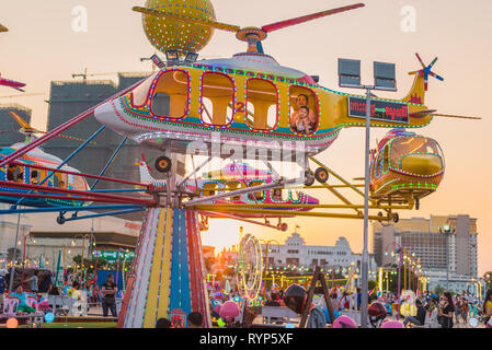 Phnom Penh, Cambodia - February 6, 2019: a young woman and a child ride the helicopter carousel in the lights of sunset at an amusement park. Stock Photo