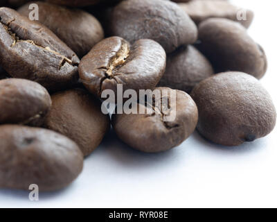 Macro image of a pile of brown, roasted coffee beans, with white background at bottom right. Stock Photo