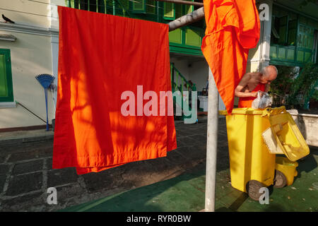 Monks' robes hung out to dry at monks dwellings in the grounds of Wat Benchamabophit, Bangkok, Thailand, an elderly monk disposing of trash Stock Photo