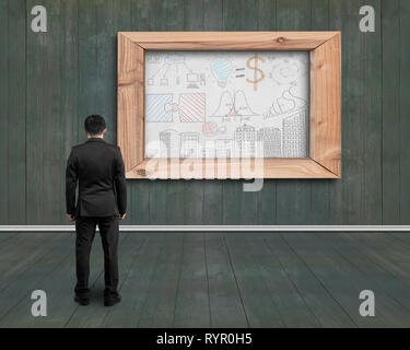 Back view businessman looking at business concept doodles drawn on white board with dark green wooden wall and floor background Stock Photo