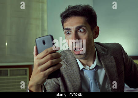 Very surprised man with tie and jacket looks at his cell. Stock Photo