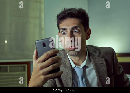 Very surprised man with tie and jacket looks at his cell. Stock Photo