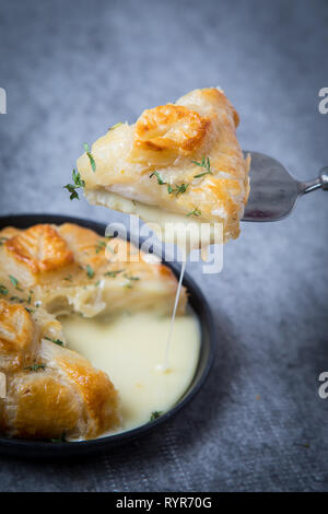 Slice of fried camembert cheese in puff pastry crust and oozing cheesy center. Camembert en croute is a traditional cheese French starter shot on a gr Stock Photo