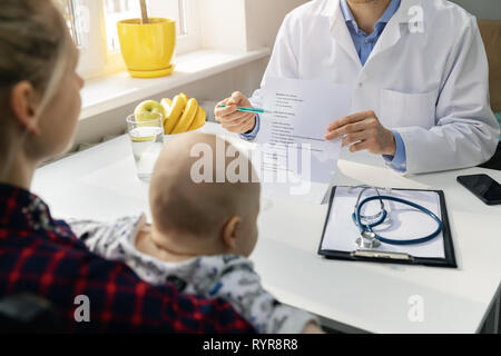 nutritionist and young mother with baby discussing healthy balanced nutrition plan in office Stock Photo