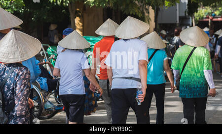 Hoi An, Vietnam - October 23, 2018: a group of Chinese tourists in Vietnamese conical hats walk in the street. Stock Photo