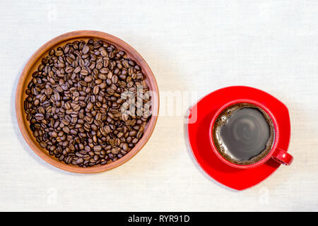 Red mug of freshly brewed coffee with roasted beans in a ceramic clay pan on linen canvas. Top view, flat lay. Stock Photo