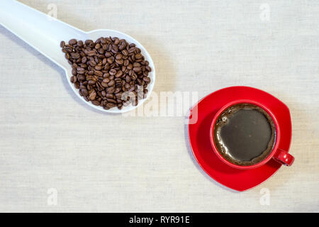 Red mug of freshly brewed coffee with roasted beans in a white spoon on a linen cloth. Top view, flat lay. Stock Photo