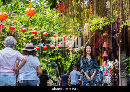 Hoi An, Vietnam - October 23, 2018: a young Asian woman poses for her friend (out of the frame) next to two strolling senior women travelers. Stock Photo
