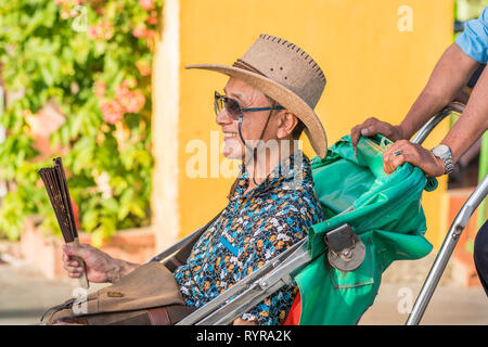 Hoi An, Vietnam - October 23, 2018: a happy smiling Asian traveler in sunglasses and hat sits in a cabin of a rickshaw against a yellow wall. Stock Photo
