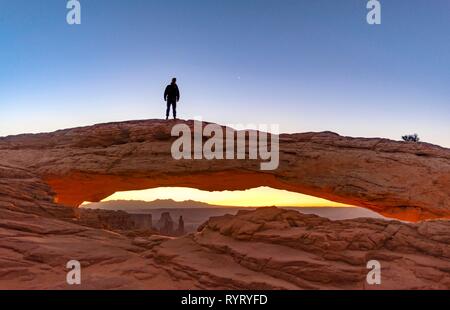Young man standing on rock arch, Mesa Arch, sunrise, Grand View Point Road, Island in the Sky, Canyonlands National Park, Moab