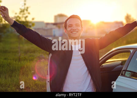 happy young man raising his hands up and smiling at sunset in the sunlight Stock Photo