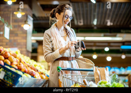 Young woman getting wallet with money while buying food in the supermarket Stock Photo