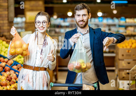 Man and woman buying food using eco and plastic bag in the supermarket. Concept of the use of eco bags during the shopping Stock Photo