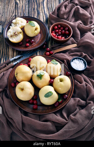 Pickled apples served on an earthenware plates with fresh mint and cranberries on an old wooden table with brown cloth and ingredients, vertical view  Stock Photo