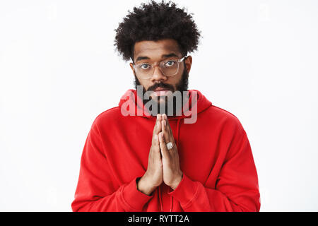 Waist-up shot of serious-looking african guy with beard holding hands in pray as asking for help being in need having troubles praying begging for Stock Photo