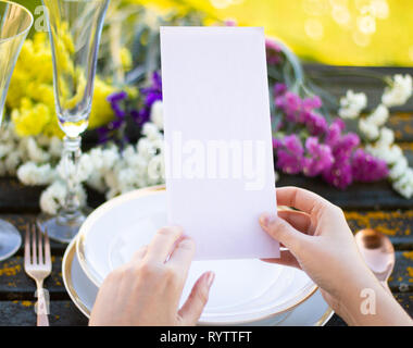 Hands holding a menu mockup on a table with tableware and flowers Stock Photo