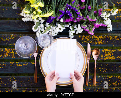 Hands holding a menu mockup on a vintage table with tableware and flowers Stock Photo